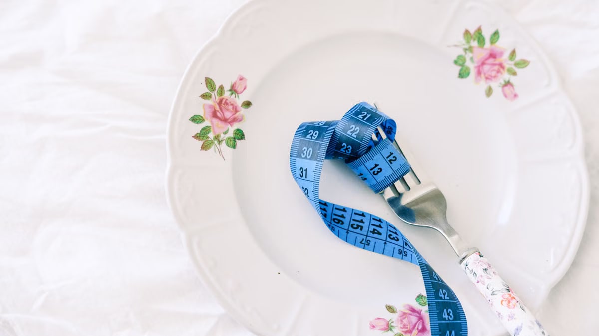 A floral plate with a blue measuring tape wrapped around a fork, symbolizing dieting.